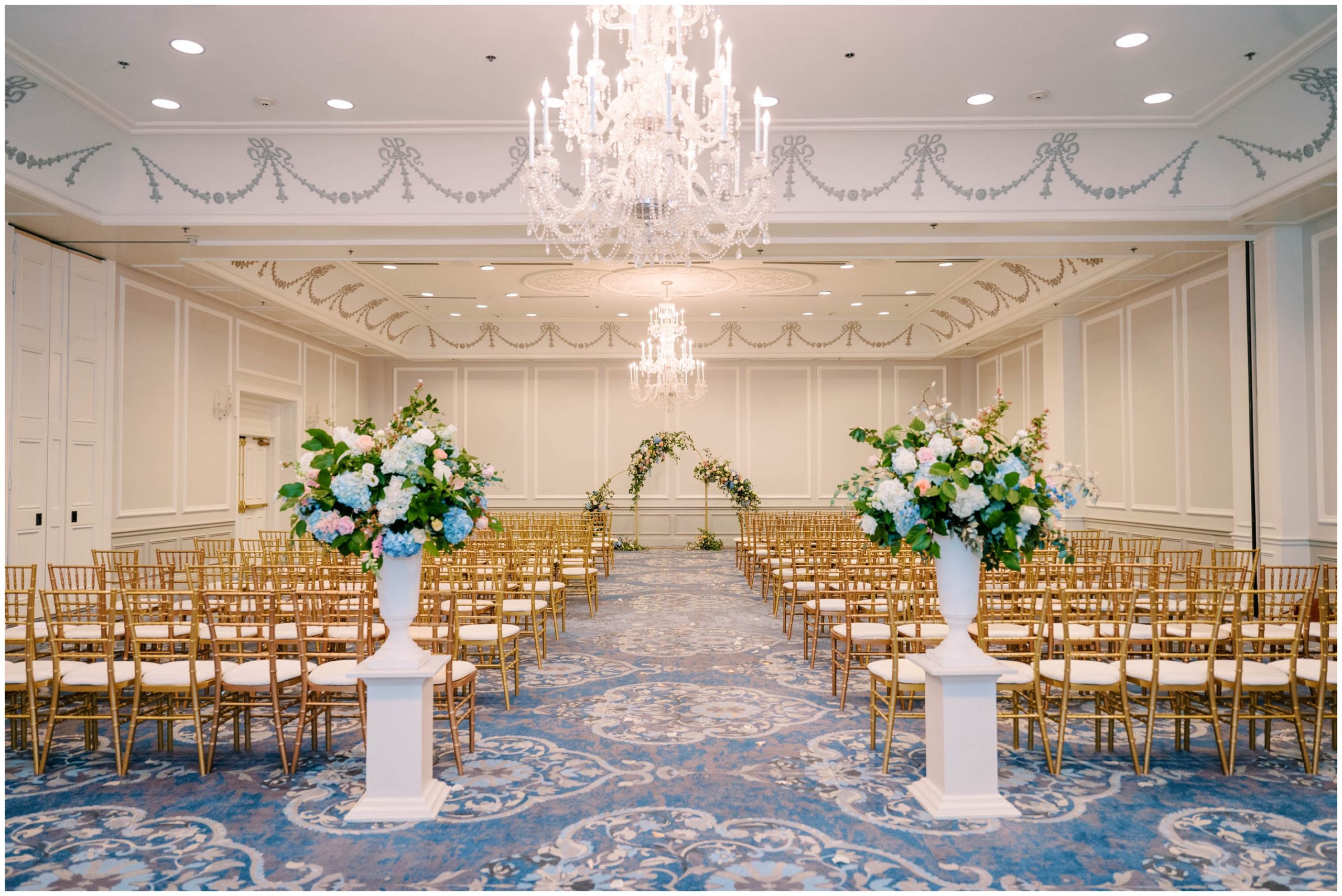 Gold Chiavari chairs, a gold archway, and pink and blue florals for a summer pastel wedding ceremony