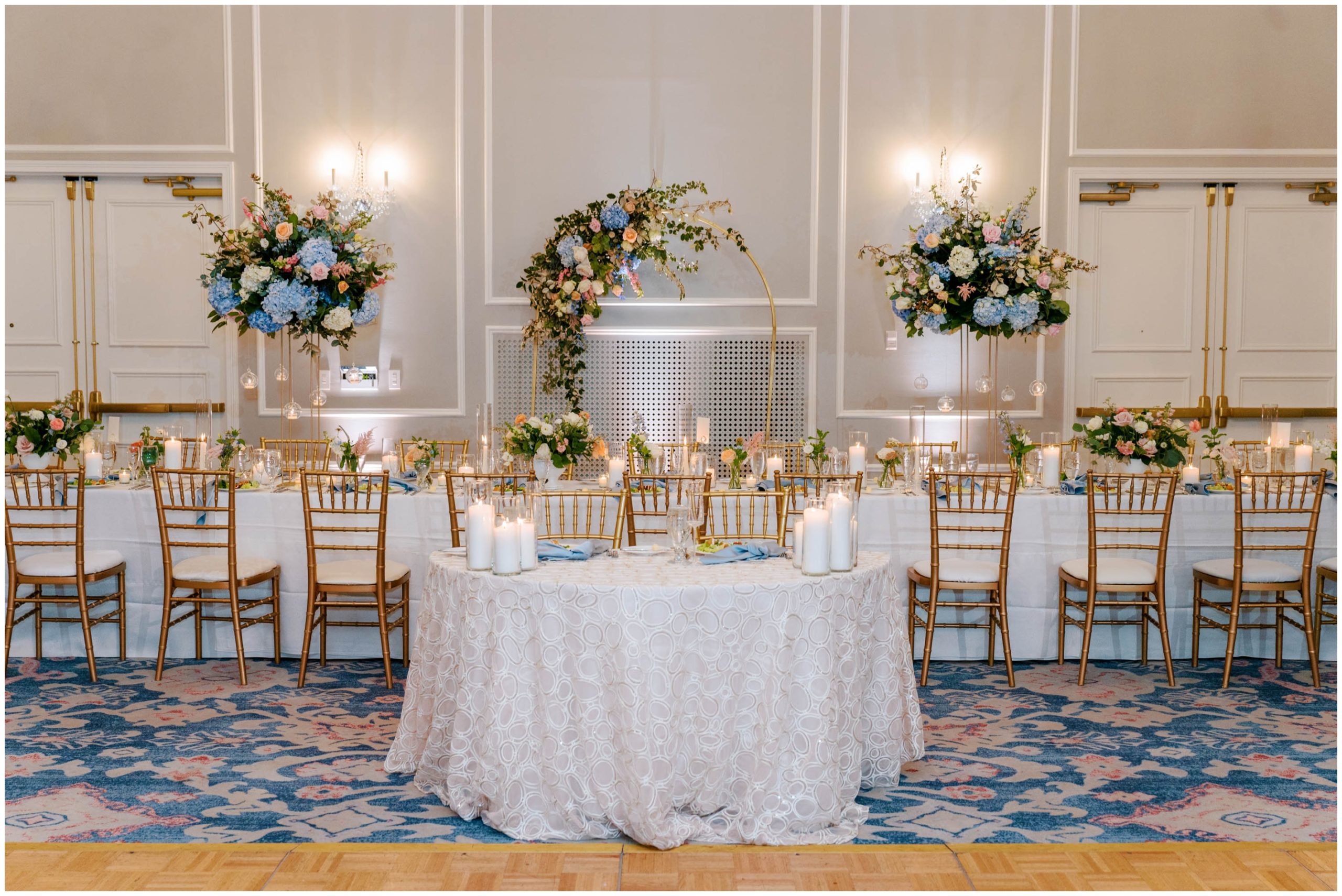 Gold Chiavari chairs, white table linens, pink and blue florals, and white pillar candles for a summer pastel wedding reception