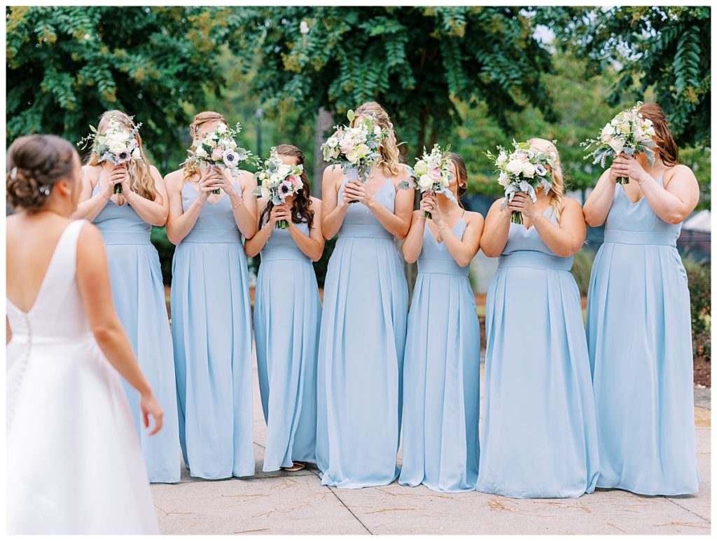 bride standing in front of bridesmaids covering their faces at the chapel hill country club