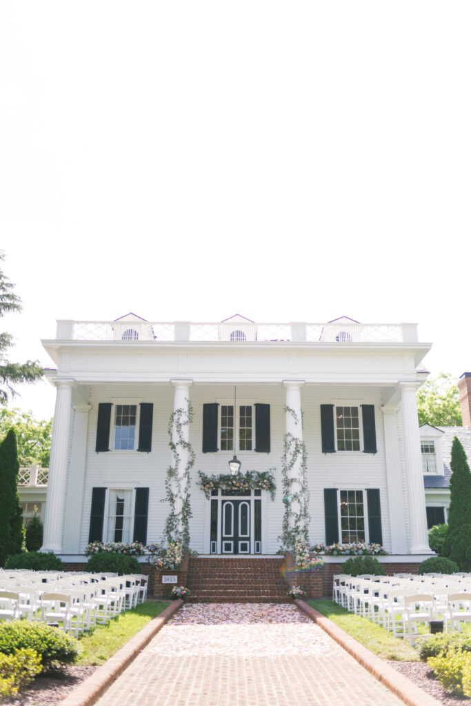 xwhimsical garden style multi colored florals with greenery wrapped around the columns for the ceremony on the front porch of Rose Hill Estate by Expression of Love Florist