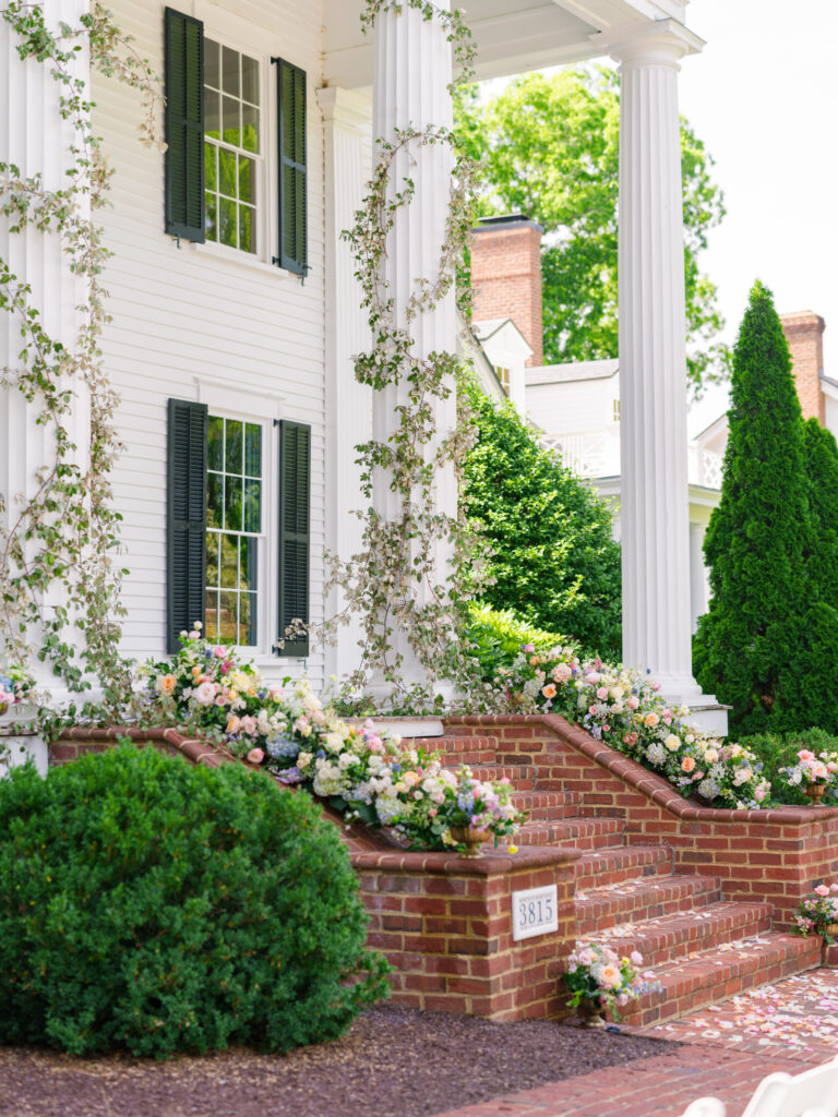whimsical garden style multi colored florals with greenery wrapped around the columns for the ceremony on the front porch of Rose Hill Estate by Expression of Love Florist