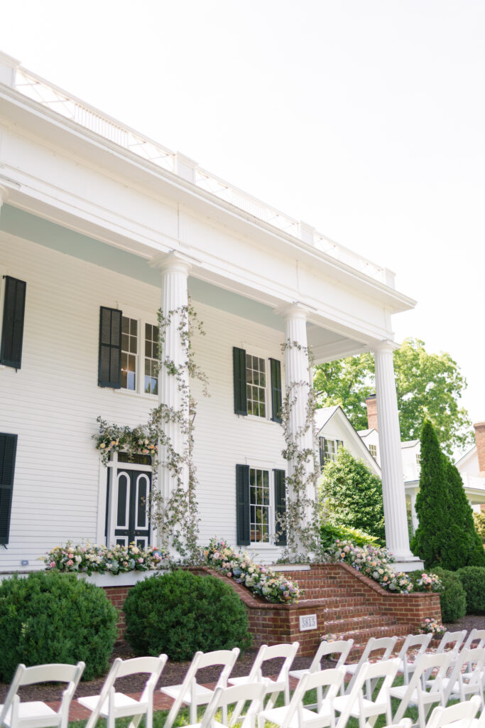 whimsical garden style multi colored florals with greenery wrapped around the columns for the ceremony on the front porch of Rose Hill Estate by Expression of Love Florist
